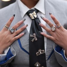 A Guest seen wearing a grey blazer jacket with blue details, black tie with silver statements and charms, silver rings, accessoires, white blouse outside Chet Lo Show during London Fashion Week February 2025 on February 23, 2025 in London, England