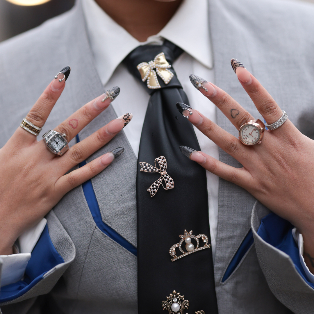 A Guest seen wearing a grey blazer jacket with blue details, black tie with silver statements and charms, silver rings, accessoires, white blouse outside Chet Lo Show during London Fashion Week February 2025 on February 23, 2025 in London, England