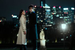 two people (Jenna Coleman as Johanna Constantine, Tom Sturridge as Dream) stand in front of a cityscape at night, in episode 103 of The Sandman.