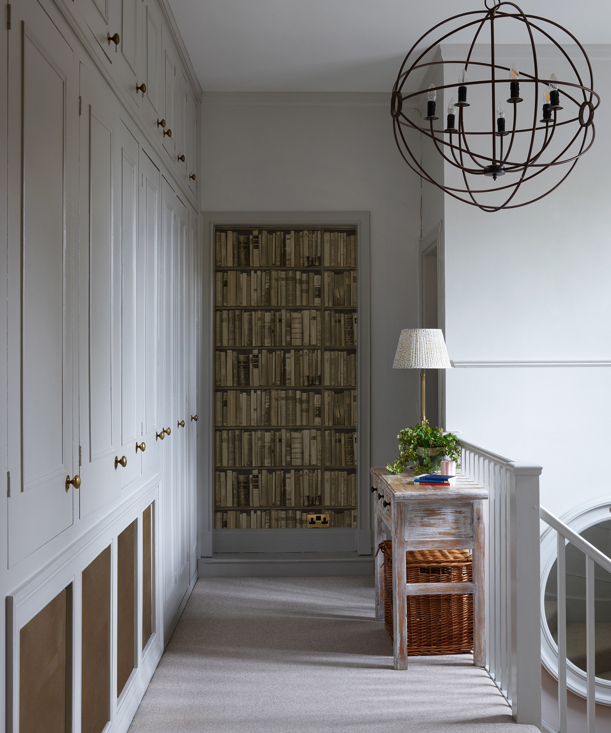 grey painted landing with fitted cabinets and faux library wallpaper at end wall