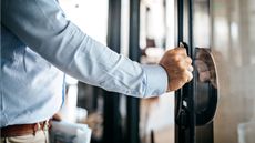 A businessman pulls open a glass office door.