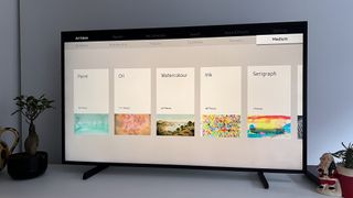 En Samsung The Frame TV 2021 står på en vit TV-bänk och visar ett utbud av olika bakgrundsbilder.