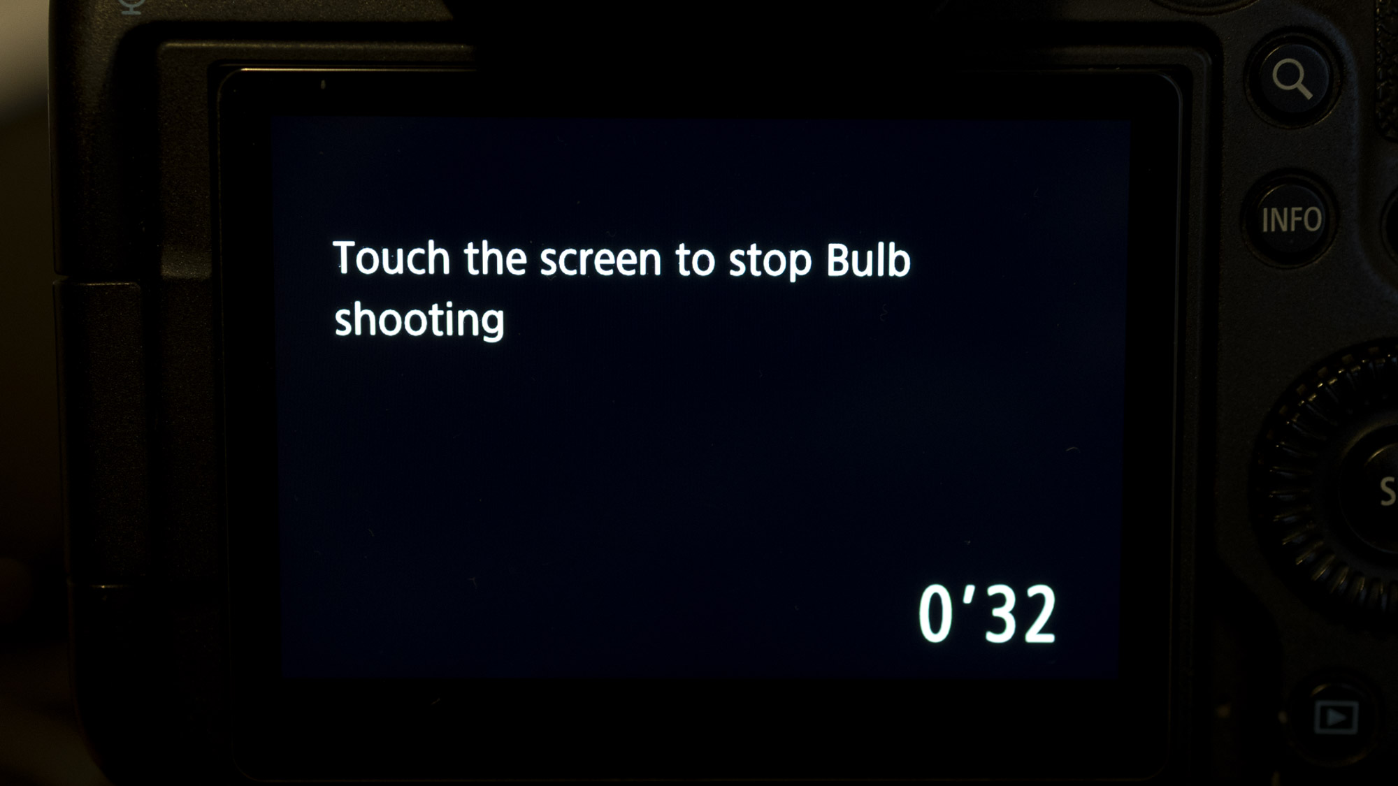 Back of a Canon EOS R5 showing the text 'Touch the screen to stop Bulb shooting' on the LCD screen. In the bottom right of the screen you can see the exposure is currently at 32 secs.