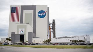 artemis 1 beside vehicle assembly building at nasa's kennedy space center with clouds in behind