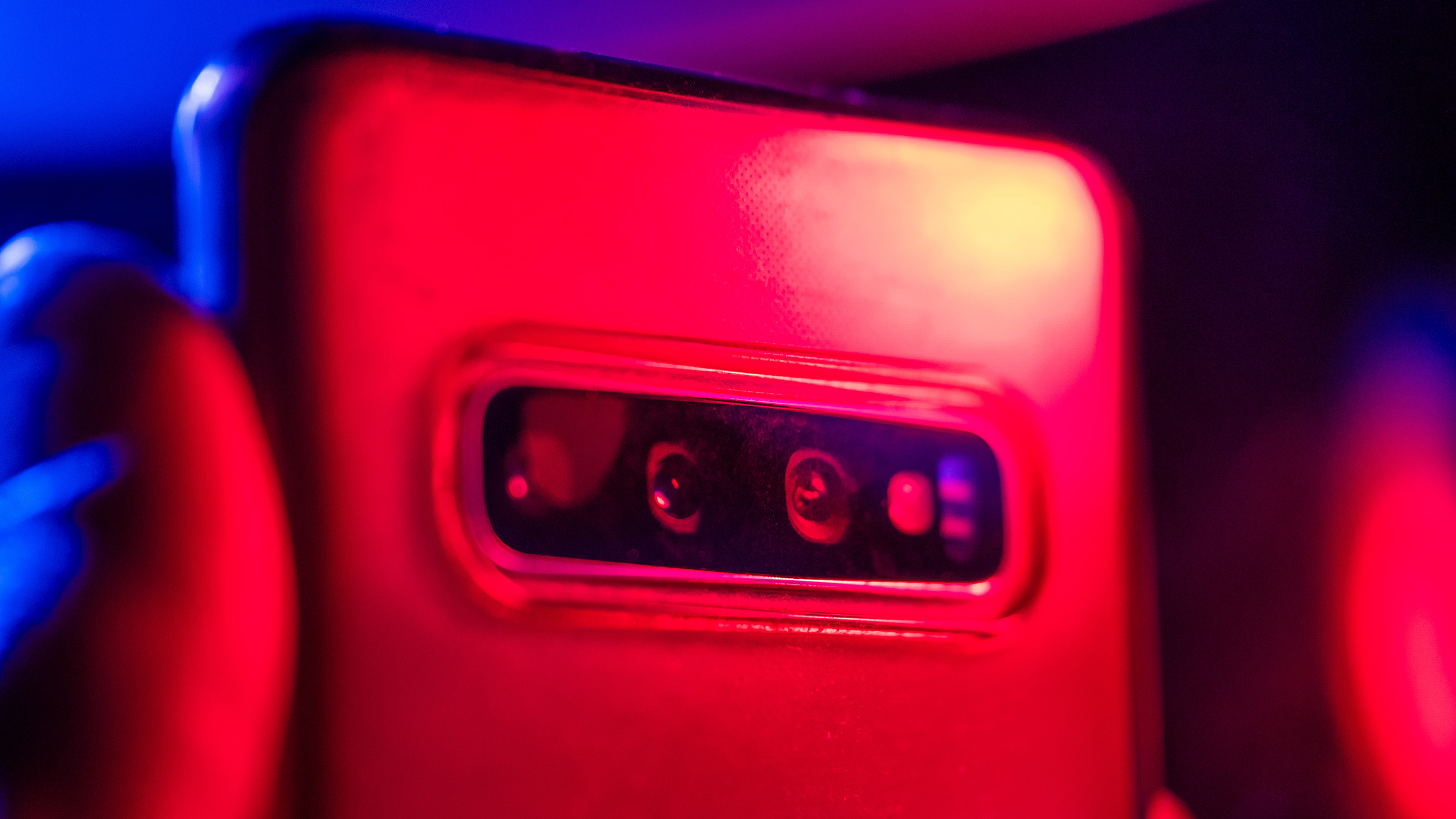 Close-up of a smartphone's rear camera lens illuminated by red and blue lights, showcasing its sleek design and glass surface