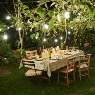 Outdoor fairy lights hanging over garden seating area in greenery