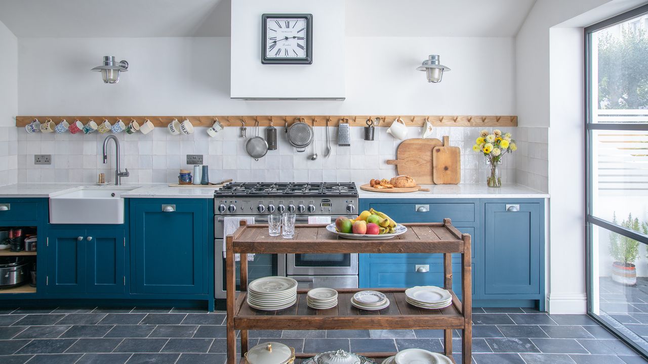 Blue kitchen with peg wall rail, slate floor tiles and crittal-style french doors