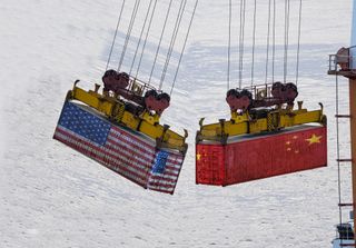 Two shipping containers hang from a crane, one is painted with the China flag, the other a USA flag