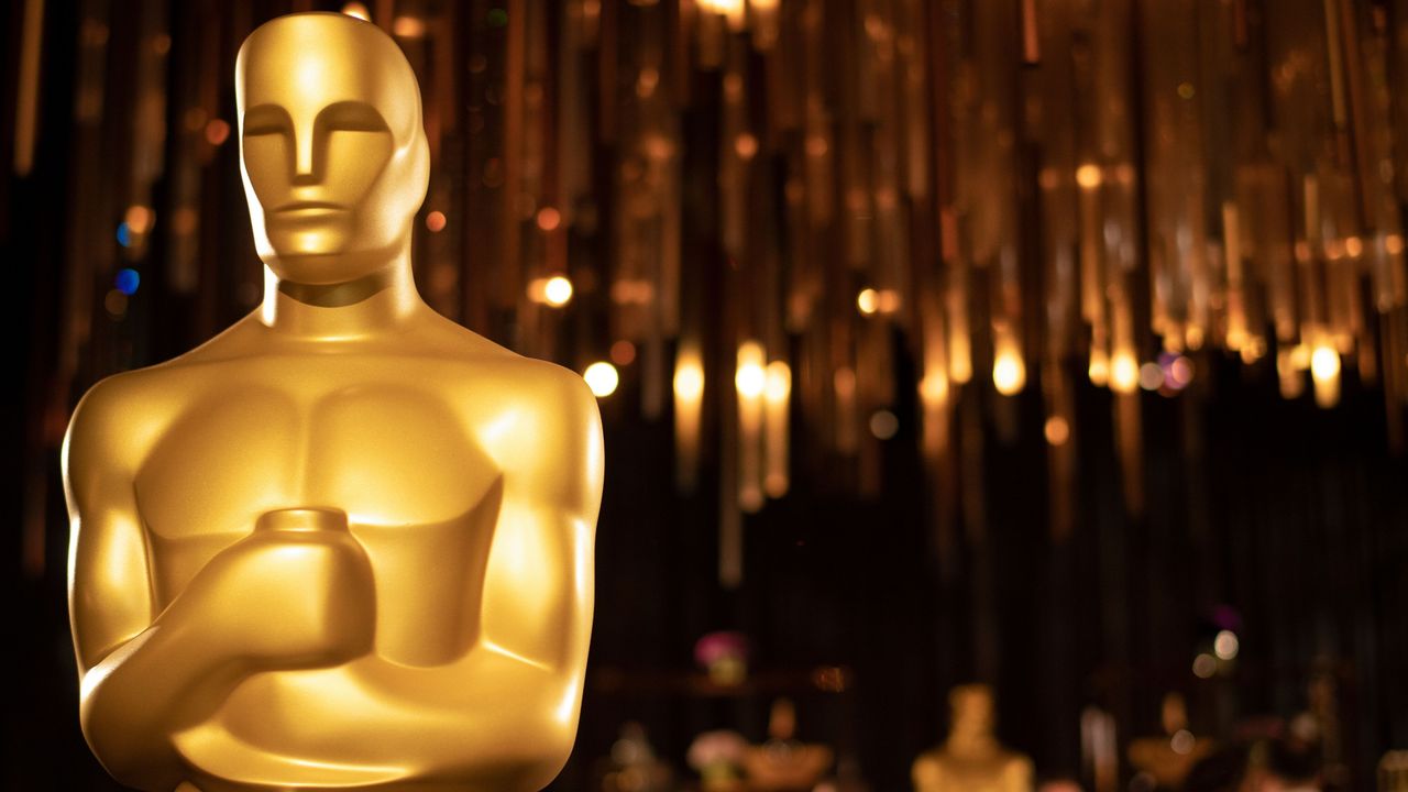 Closeup of an Oscar award with the ceremony in the background.