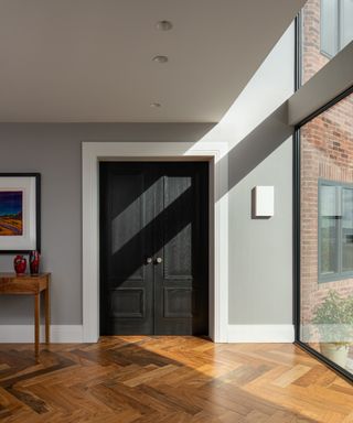 entrance hall with large double height window, grey walls, black internal door and wooden flooring