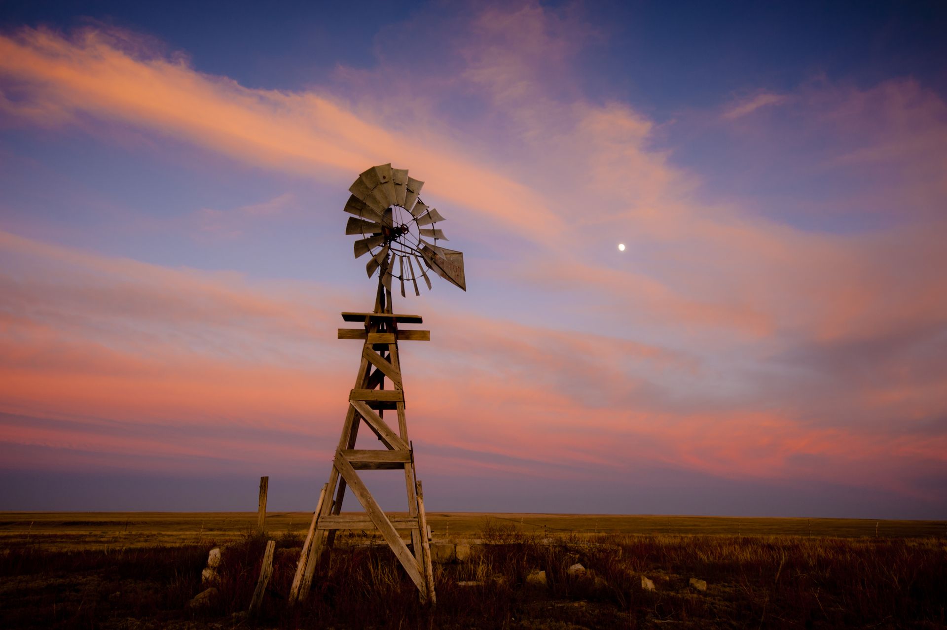 An old wooden windmill at sunset with a pink sky and the moon above. Lamar, Colorado, USA.