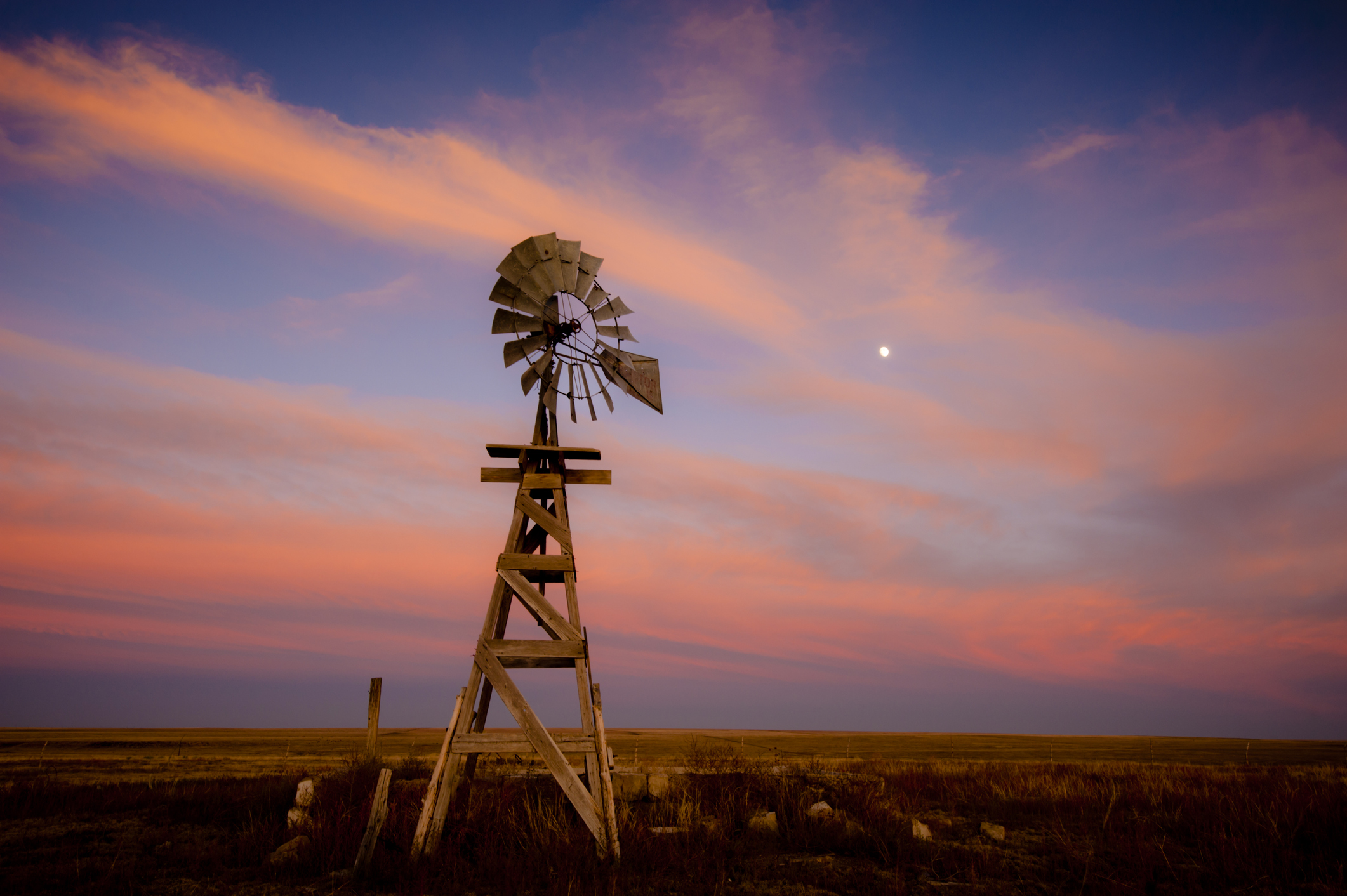 An old wooden windmill at sunset with a pink sky and the moon above. Lamar, Colorado, USA.