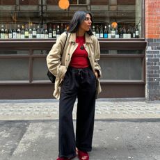 An image of @monikh wearing a red top with black joggers, red sandals and a beige jacket while in London.