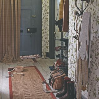 A hallway covered in a botanical wallpaper with a jute rug with a red border laid down on the wooden floor