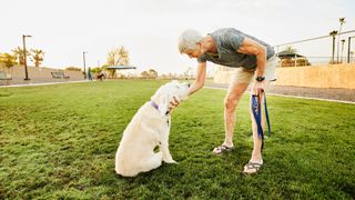 Senior woman petting dog under chin during early morning walk in dog park