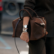 WOMAN carrying a brown suede bag with silver cuff bracelets
