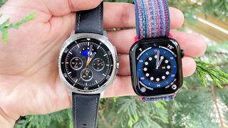 Close up of the Samsung Galaxy Watch Ultra 8 and Apple Watch Series 10 next to each other against a green, foliage background