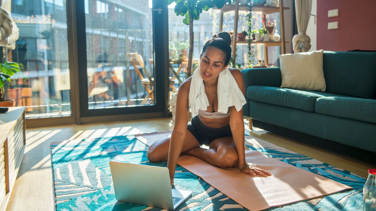 A young woman exercises at home using a laptop 