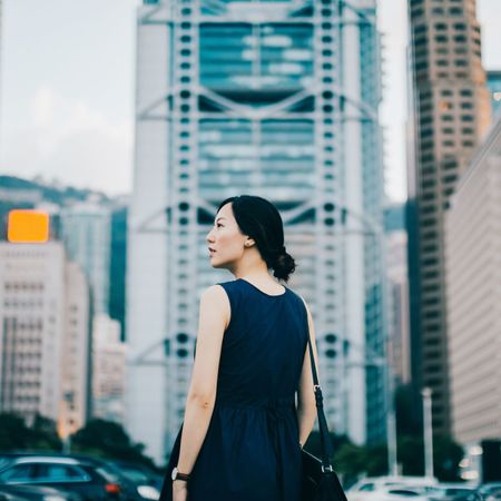 Successful young businesswoman looking away with confidence standing against urban cityscape