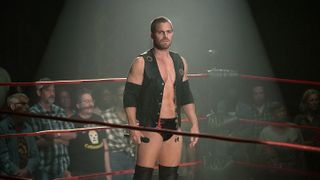 Jack (Stephen Amell) standing alone in the wrestling ring in Heels season 2, with fans at ringside, holding a microphone.