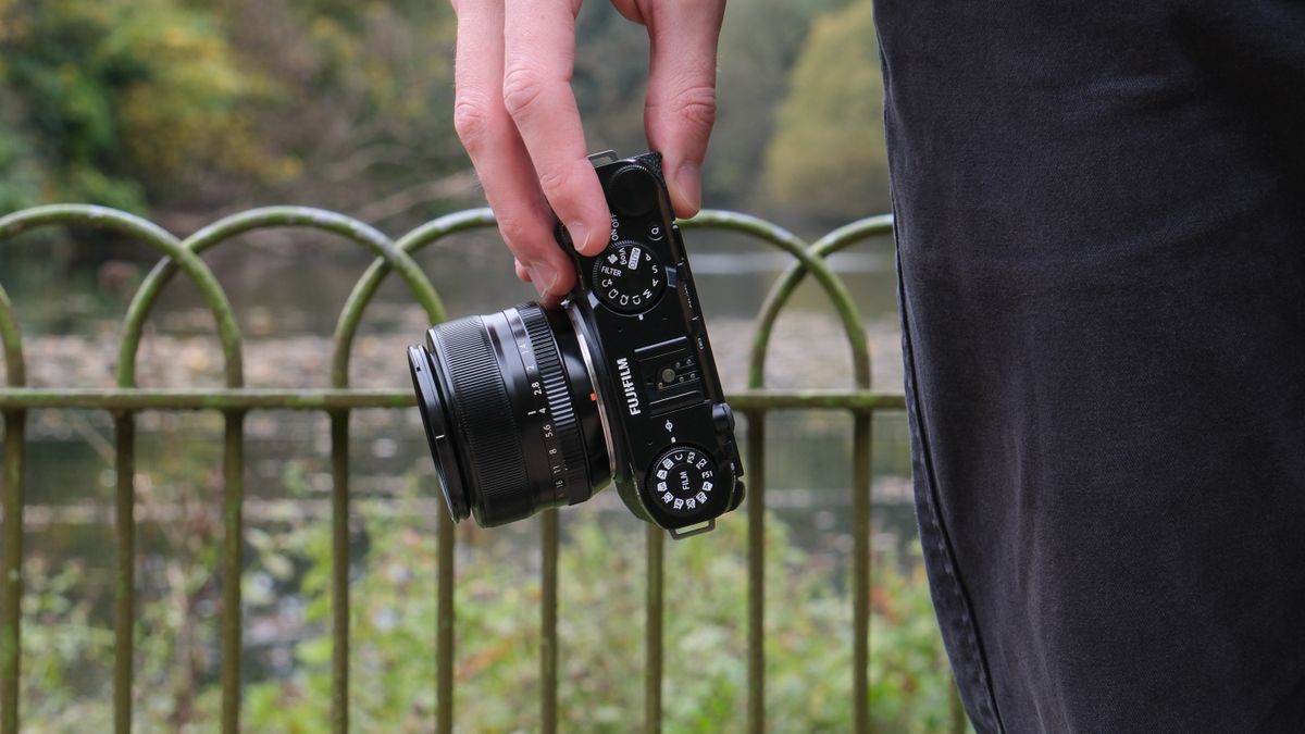 Fujifilm X-M5 camera with a Fujifilm 35mm lens attached held in a hand in front of a lake