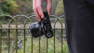 Fujifilm X-M5 camera with a Fujifilm 35mm lens attached held in a hand in front of a lake