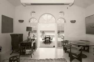 Large room with table and chairs opposite an ornate desk with chair. Glass doors open to a veranda with table and chairs