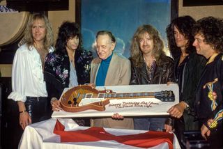 American rock band Aerosmith (L-R Bassist Tom Hamilton, Singer Steven Tyler, American Guitarist Les Paul, Guitarist Brad Whitford, Guitarist Joe Perry and Drummer Joey Kramer) host a party for Les Paul celebrating his 75th birthday. Seen here with Les Pauls birthday cake on June 12, 1990 at The Hard Rock Cafe in New York City, New York.