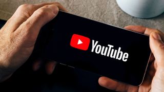 Man holding a smartphone with the YouTube app opening