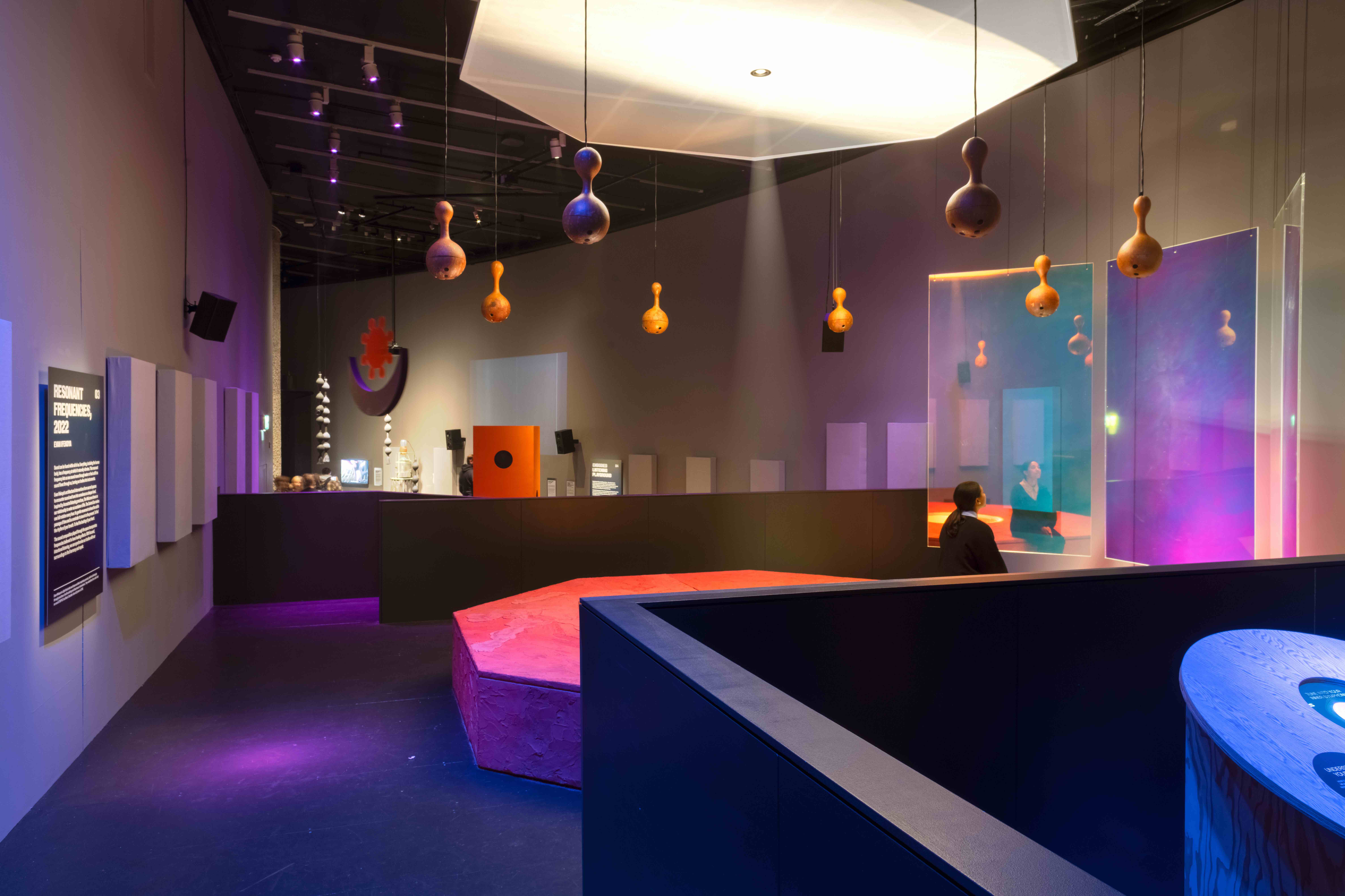 Gallery exhibition space with coloured lighting and speakers hanging from ceiling