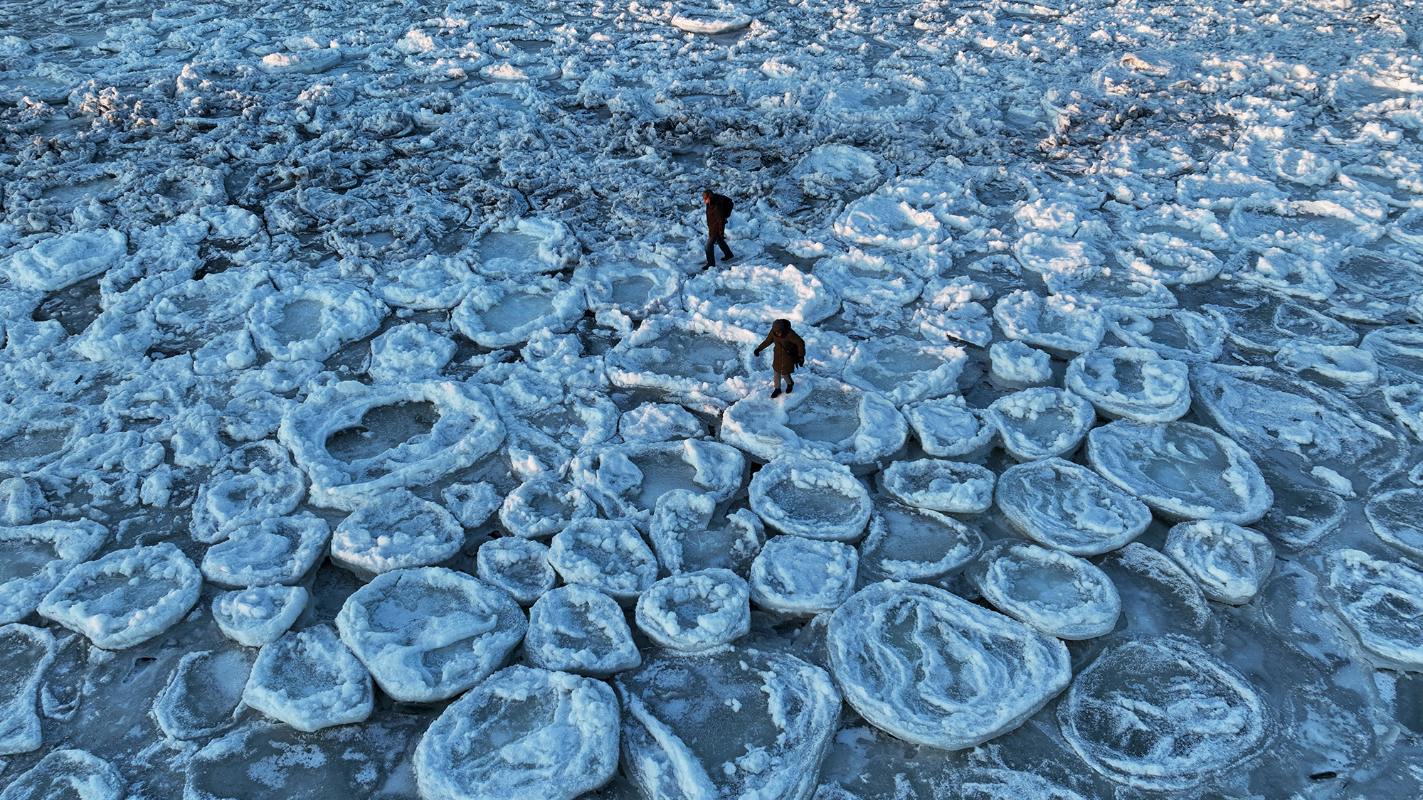 People walk across pancake ice formations in the Baltic Sea near Mikoszewo, Poland
