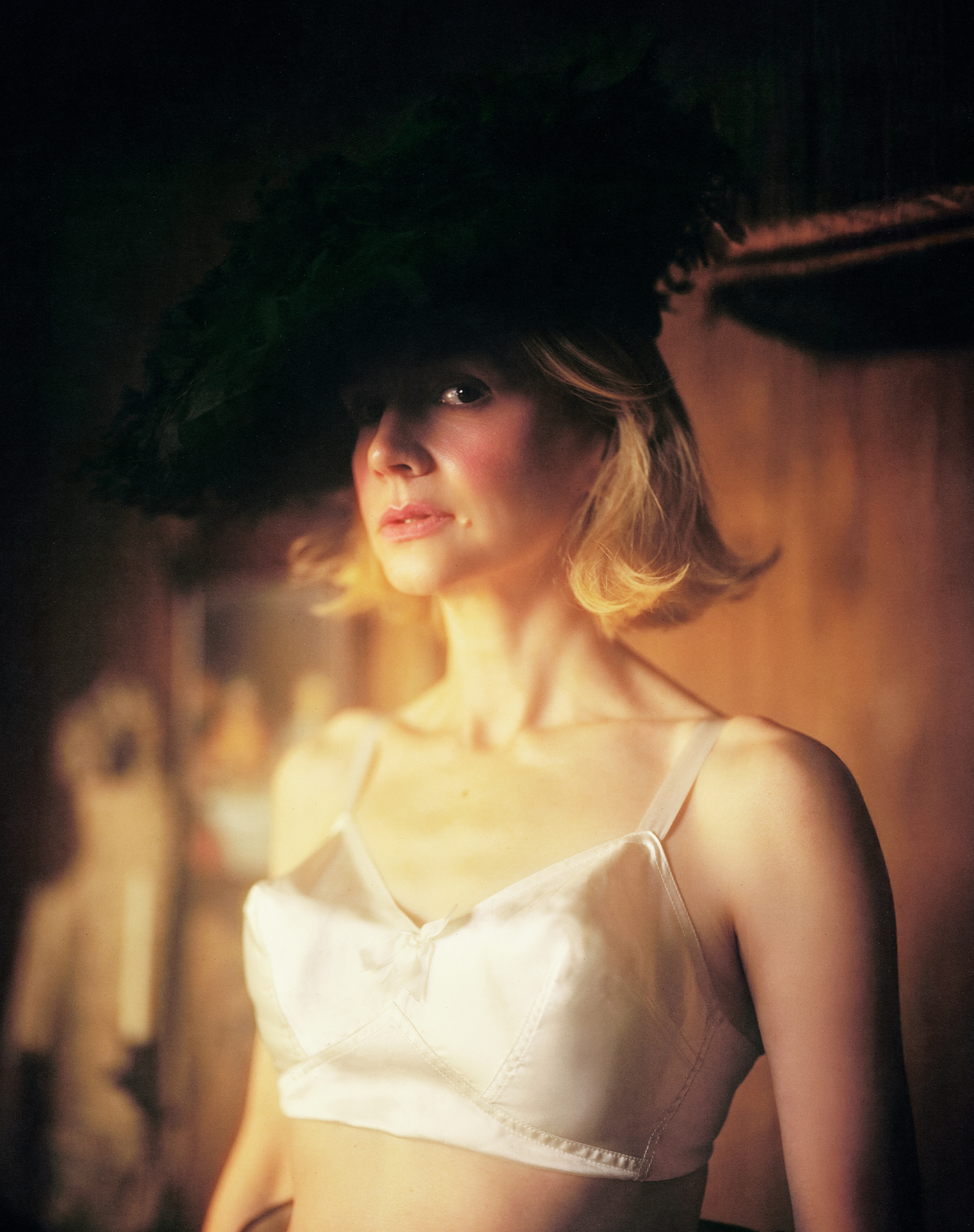 Carey Mulligan for Who What Wear's April cover story wearing a white silk bra and a feathery black hat titled sideways.