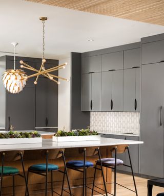 Gray kitchen with gray cabinets floor to ceiling, island with bright bar stools, tiled backsplash, metallic pendant lights, wooden floor