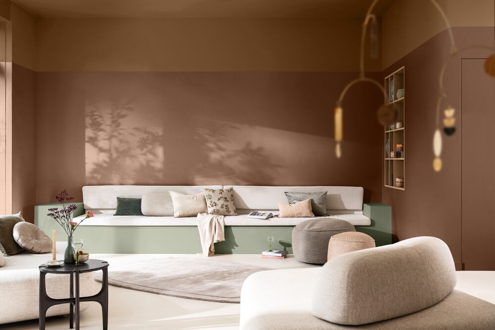 A living room with terracotta brown and ochre yellow colorblock walls with a built-in bench seat sofa that's base is painted sage green.