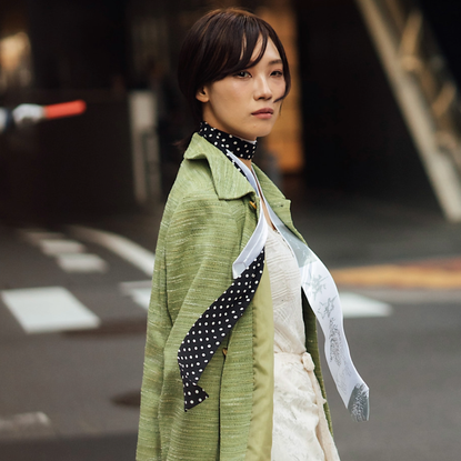 woman wearing a green jacket, polka-dot scarf, and white shirt. 