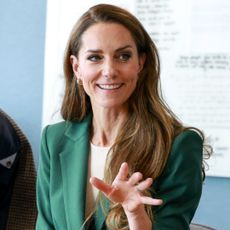 Princess kate sitting at a table wearing a green suit and talking to a man and woman in front of a whiteboard
