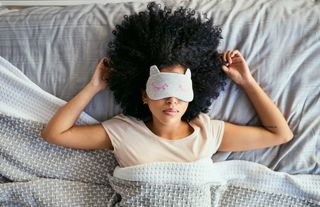 A woman wearing an eye mask sleeps on her back