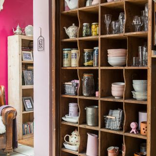Wall of wooden shelving to hold kitchenware in a pink kitchen