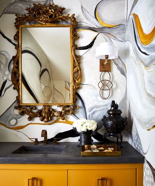 Colorful powder room with abstract wallpaper, yellow cabinet, metal mirror