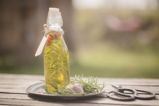A bottle of rosemary-infused olive oil on a garden table, next to a sprig of rosemary and garden scissors