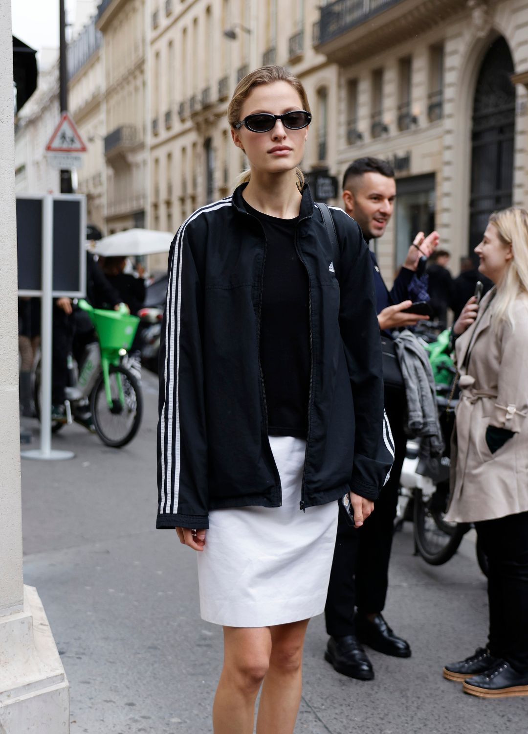 A guest wears black Adidas jacket, white mini skirt, black ballet flats, outside The Row, during Womenswear Spring/Summer 2025 as part of Paris Fashion Week on September 25, 2024 in Paris, France.