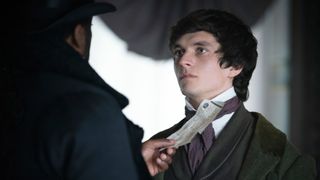 Jaggers (Ashley Thomas) holds a piece of paper to Pip's (Fionn Whitehead) throat in Great Expectations