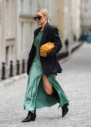 Justyna Czernia wears sunglasses, gold earrings, a green mint satin silk slit / split long dress, a black oversized blazer jacket, an orange shiny leather puffy handbag from Bottega Veneta, black shiny leather pointed high boots, gold ring, outside Alexis Mabille, during Paris Fashion Week - Haute Couture Spring/Summer 2022, on January 25, 2022 in Paris, France