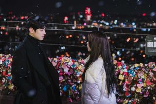 A man and a woman stand on the love lock bridge at N Seoul Tower, in 'True Beauty.'