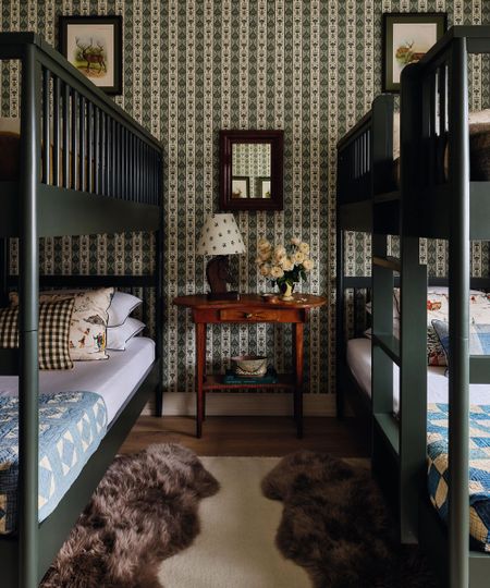 a green floral wallpapered bedroom with two dark green bunk beds, layered rugs, plaid pillows and patchwork blankets style the beds