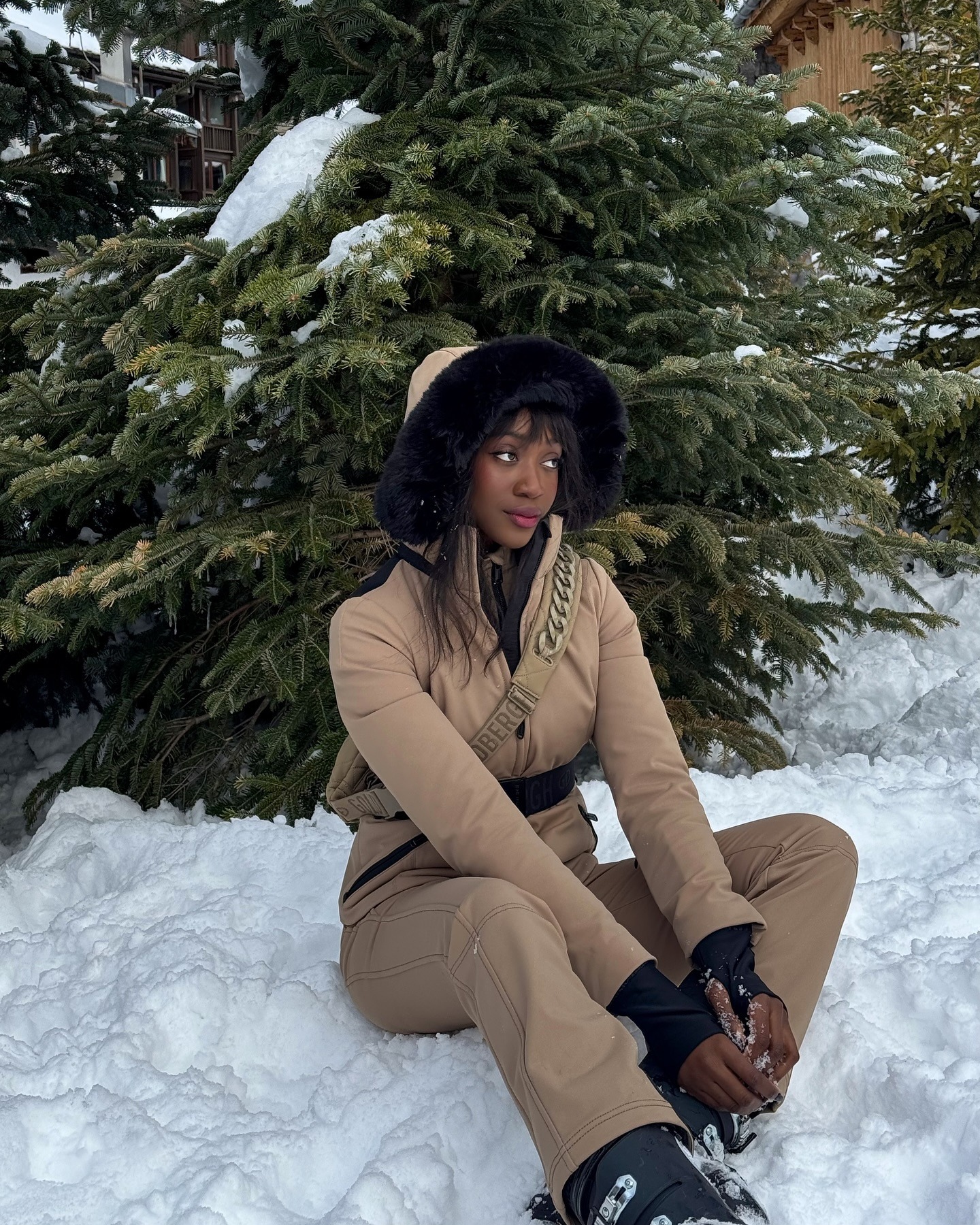 @emmanuellek_ in a ski suit sitting next to a pine tree in the snow