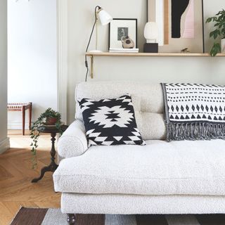 Grey boucle sofa with grey aztec cushion and throw over the back of it, with white walls behind it