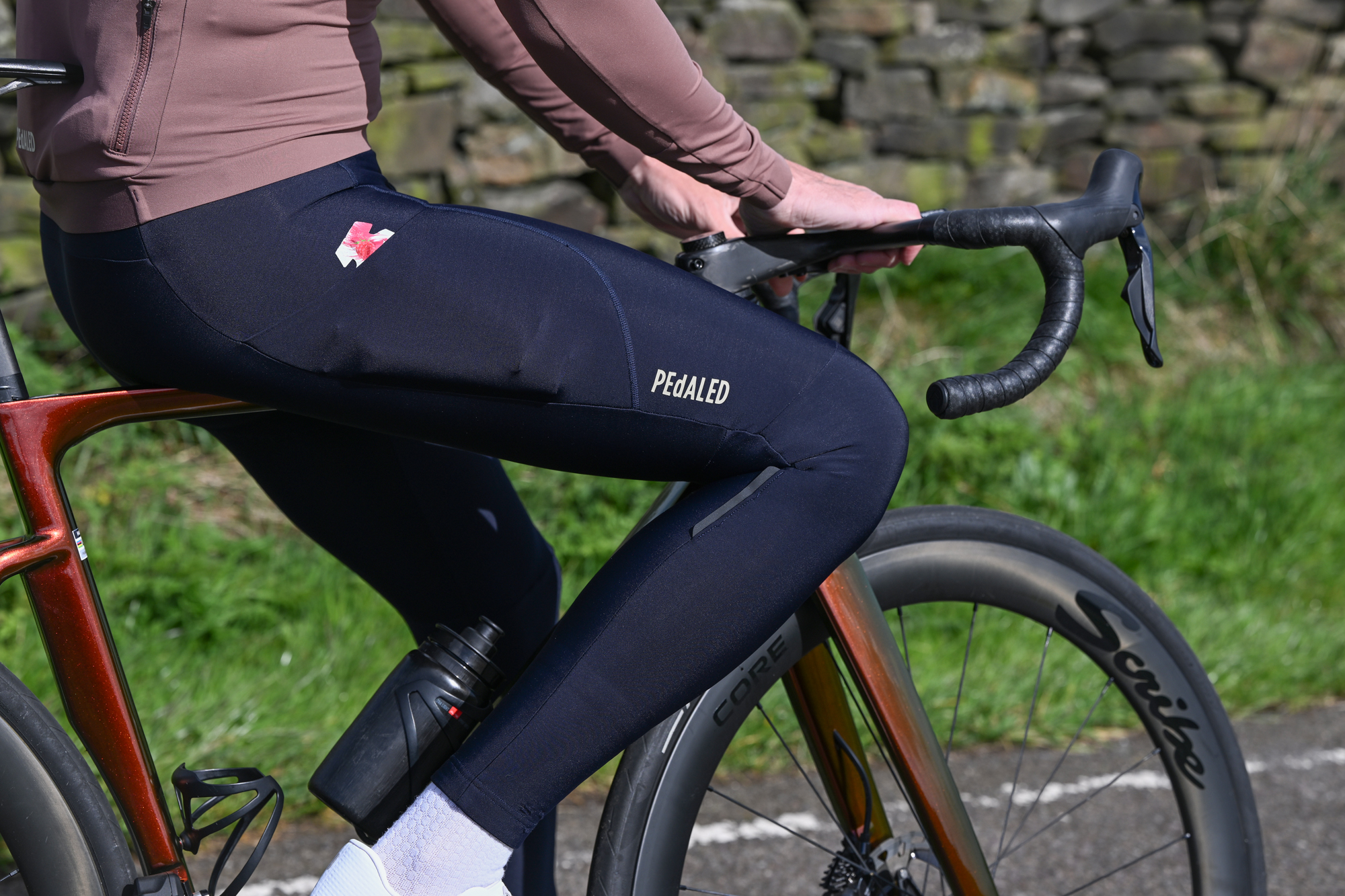 Man sitting on the top tube of an orange bike wearing dark blue tights and white shoes