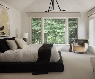 bedroom with black upholstered bed cream walls and large windows and views of trees