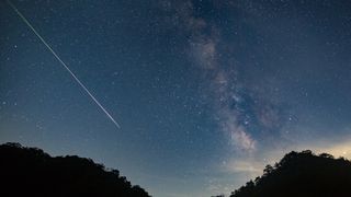 A meteor shoots across the night sky sky leaving a trail of light across the milky way